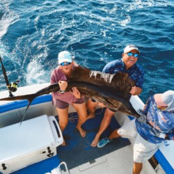 Guests and crew holding a sailfish aboard a fishing boat in Cancun.